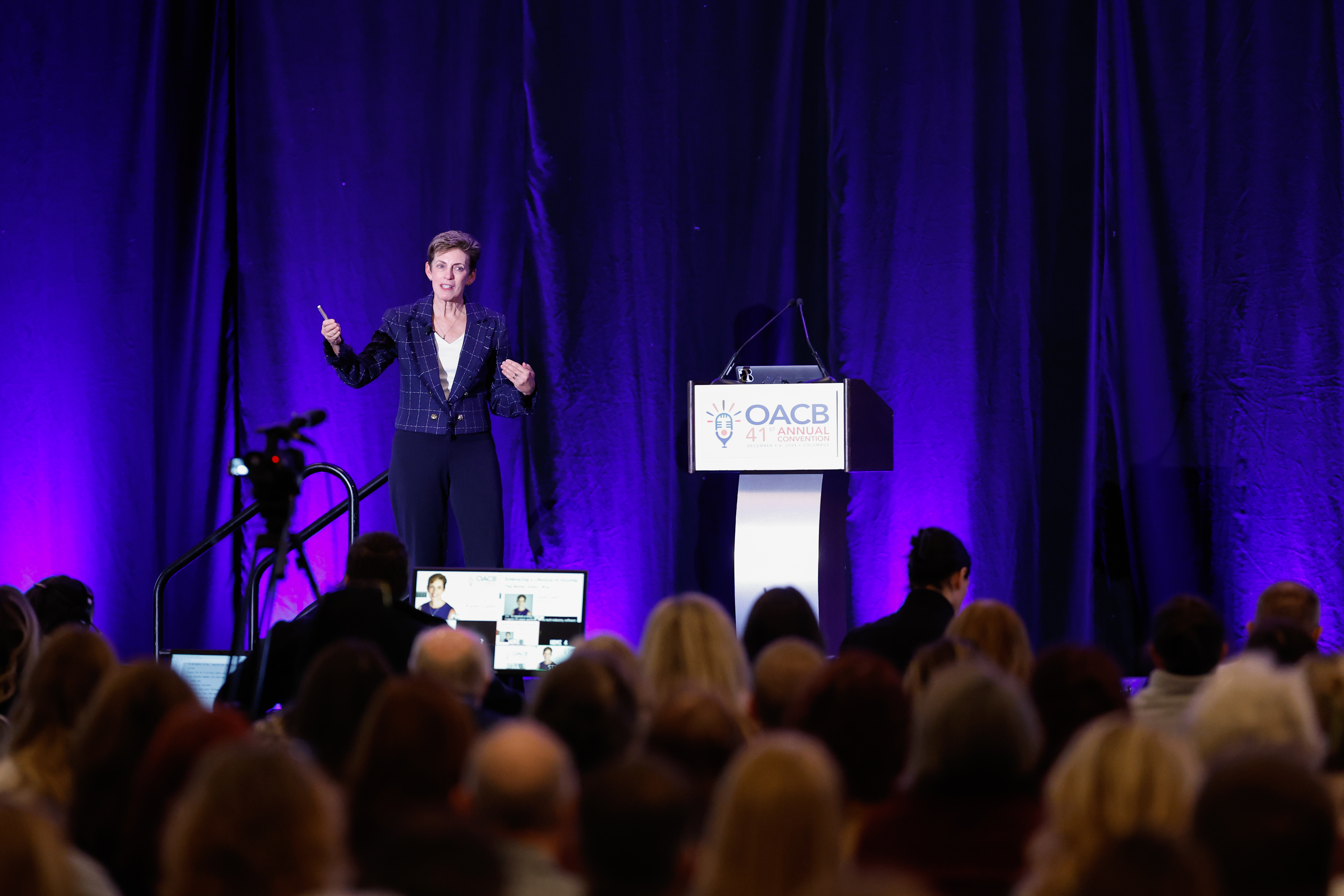 Photo of Karen speaking at the OACB annual convention. She is using hand gestures to illustrate her point in front of a large audience.